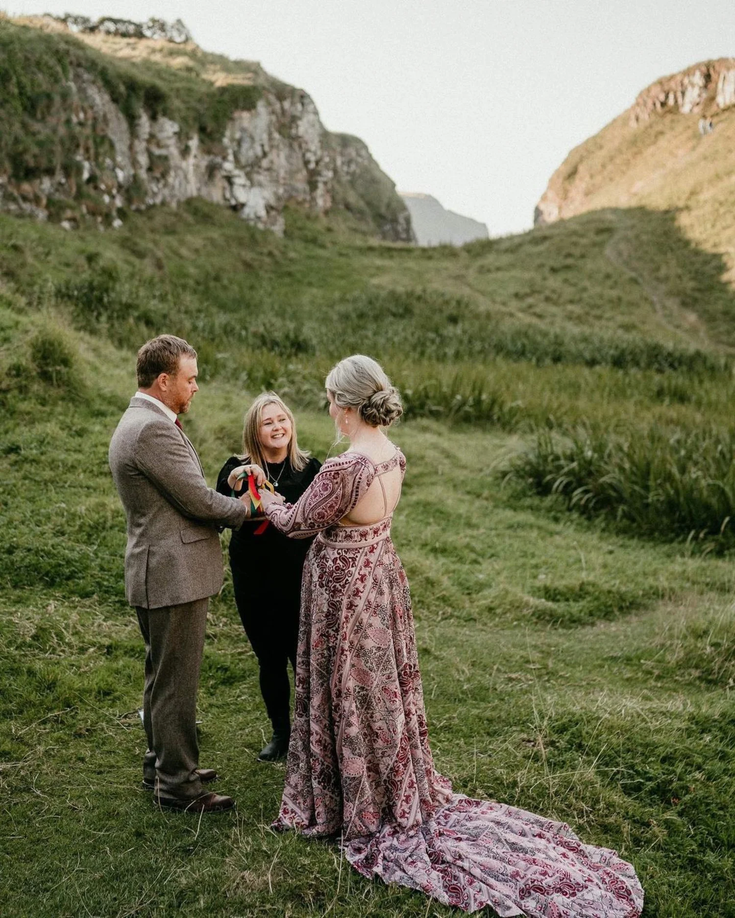 A couple being married in by cliffs in Ireland, a small blonde lady smiles up at the bride.